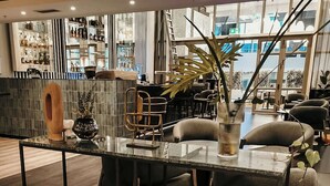 Zona de bar moderna con mostrador de vidrio, asientos y un amplio ventanal con vistas a la ciudad.