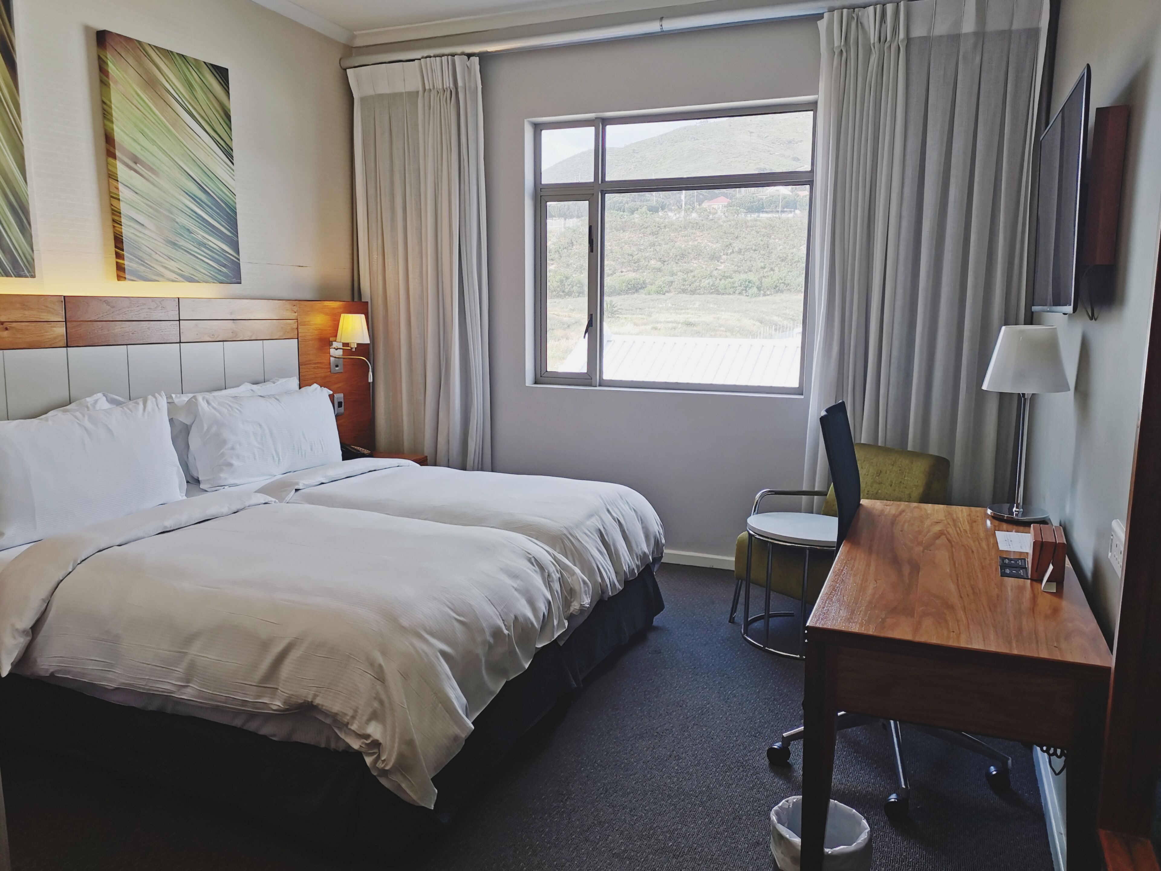 A hotel room with a large bed, a desk, a chair, a TV, and a window with a view of the outdoors.