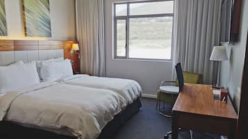 A hotel room with a large bed, a desk, a chair, a TV, and a window with a view of the outdoors.