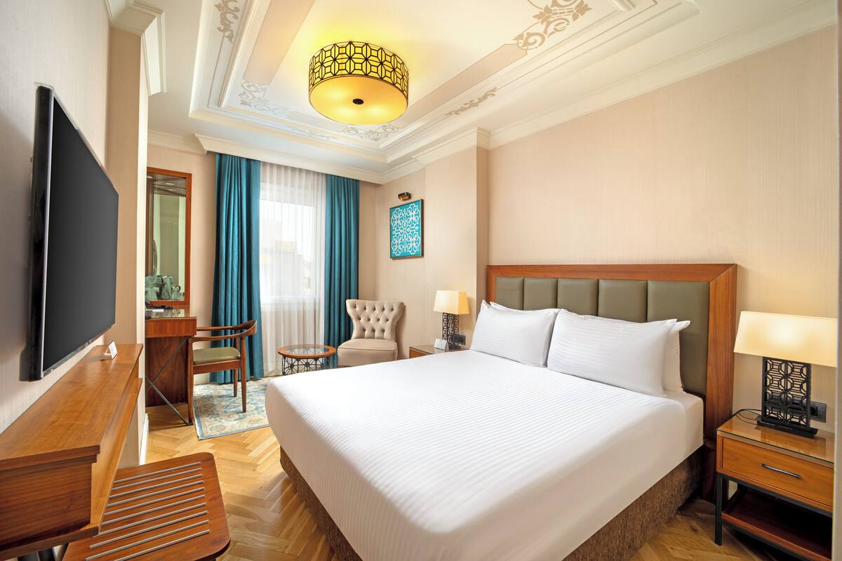 A hotel room with a large bed, a TV, a desk, a chair, and a small table.