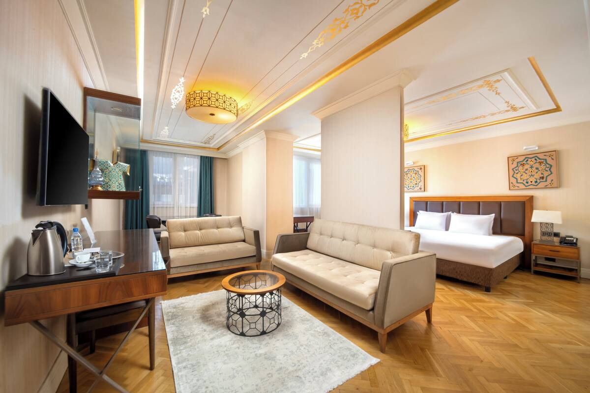 A hotel room with a bed, two sofas, a TV, a desk, and a coffee table.