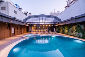 A modern indoor pool area with a glass-enclosed bar and lounge seating.