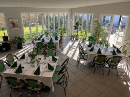 Comedor con mesas dispuestas para varios comensales, rodeado de amplios ventanales con vistas al exterior.