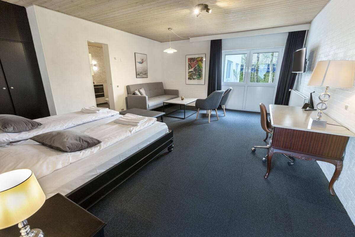 A modern hotel room with a bed, a sofa, a desk, and a chair.