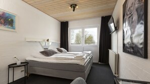A hotel room with a bed, a small table with a vase, a window with curtains, and a poster on the wall. - Dolphin Hotel Herning (Herning)