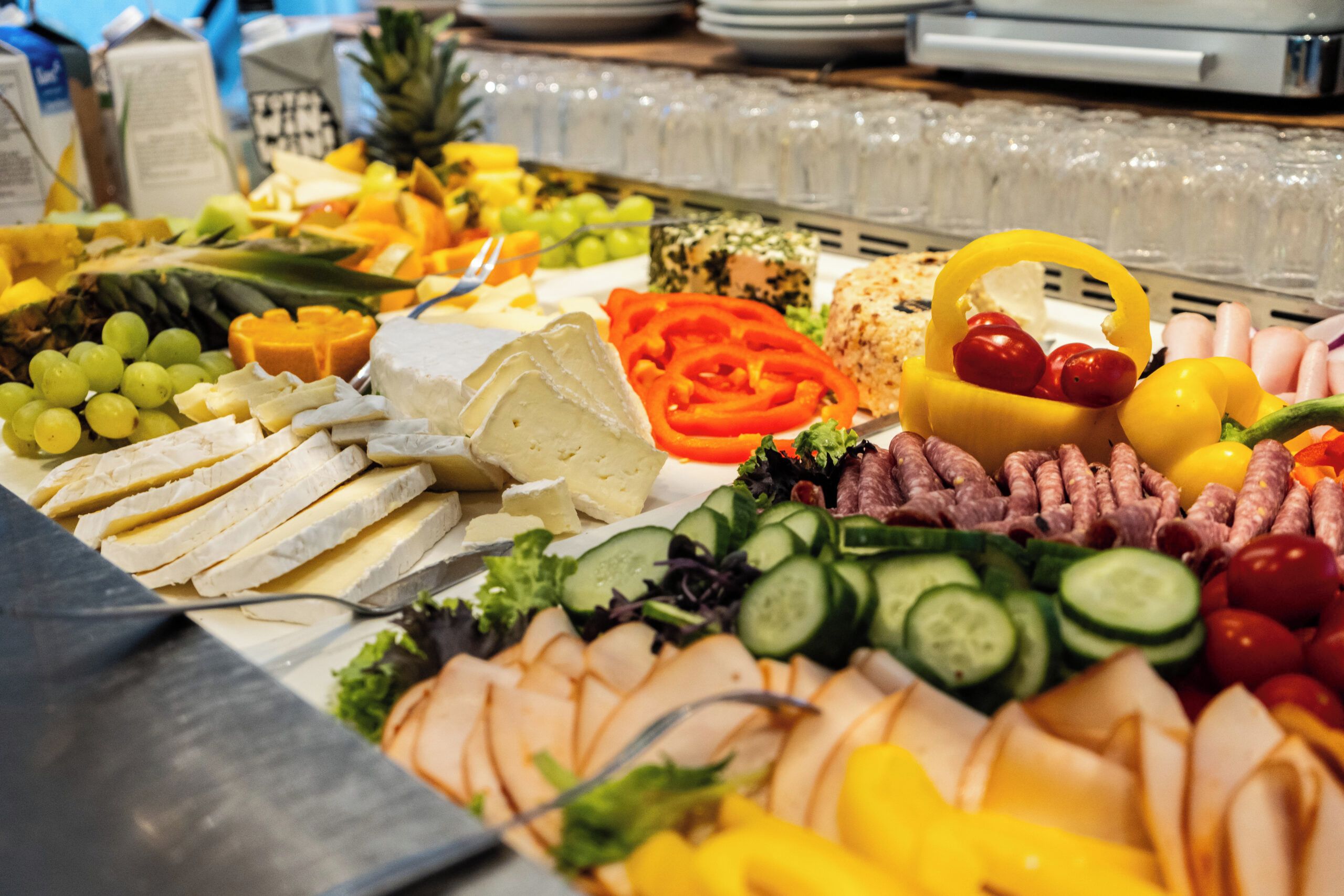A buffet with various cheeses, fruits, vegetables, and meats.
