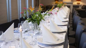 A long dining table set with white tablecloths, napkins, and glassware, with floral centerpieces and candles.
