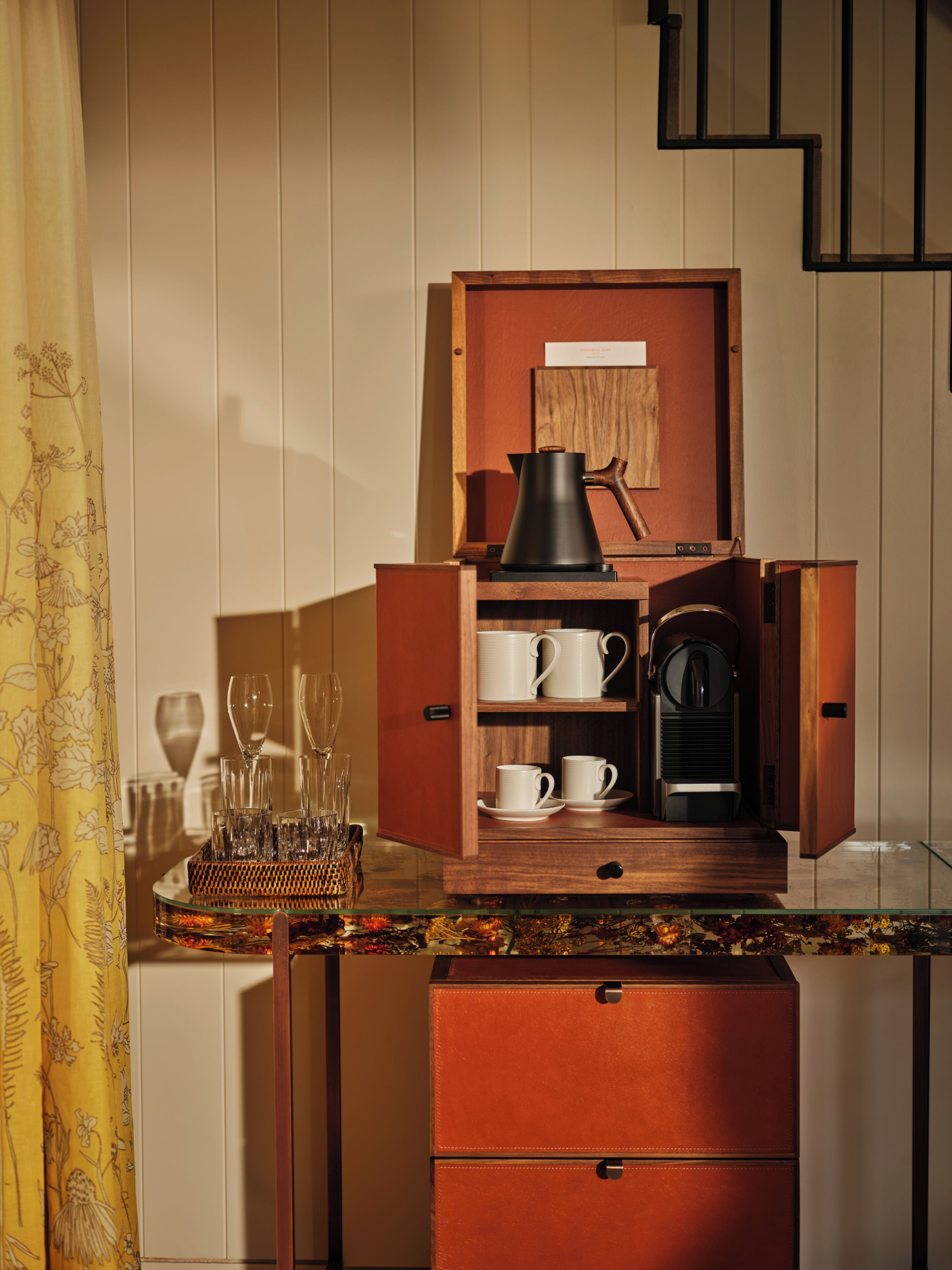 A compact kitchen with a coffee maker, cups, and a wine glass set.
