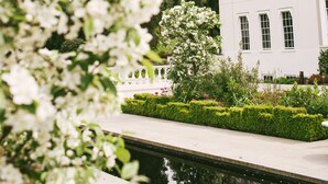 A white building with multiple windows and a garden with a water feature. - Coworth Park - Dorchester Collection (Ascot)