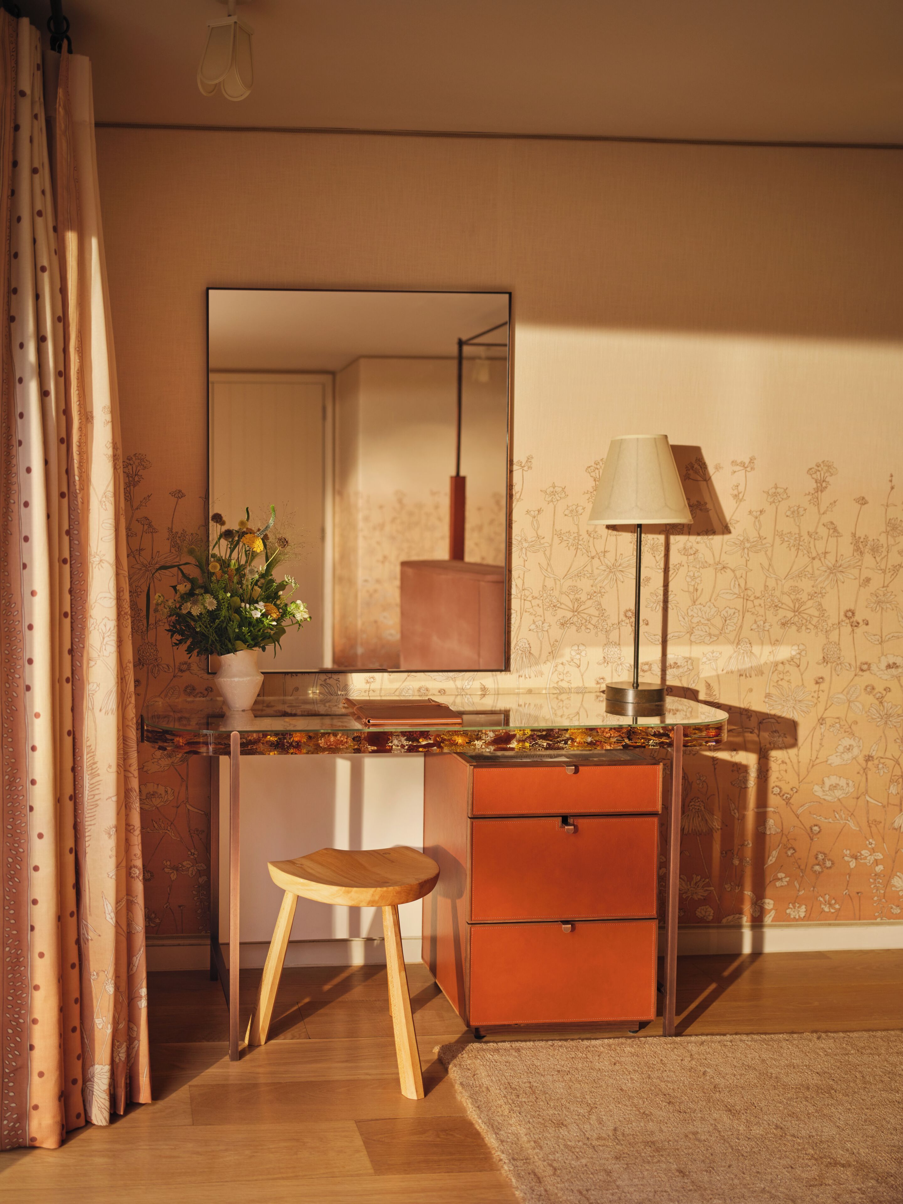 A modern bathroom with a glass shower enclosure, a wooden stool, a mirror, and a floor lamp.