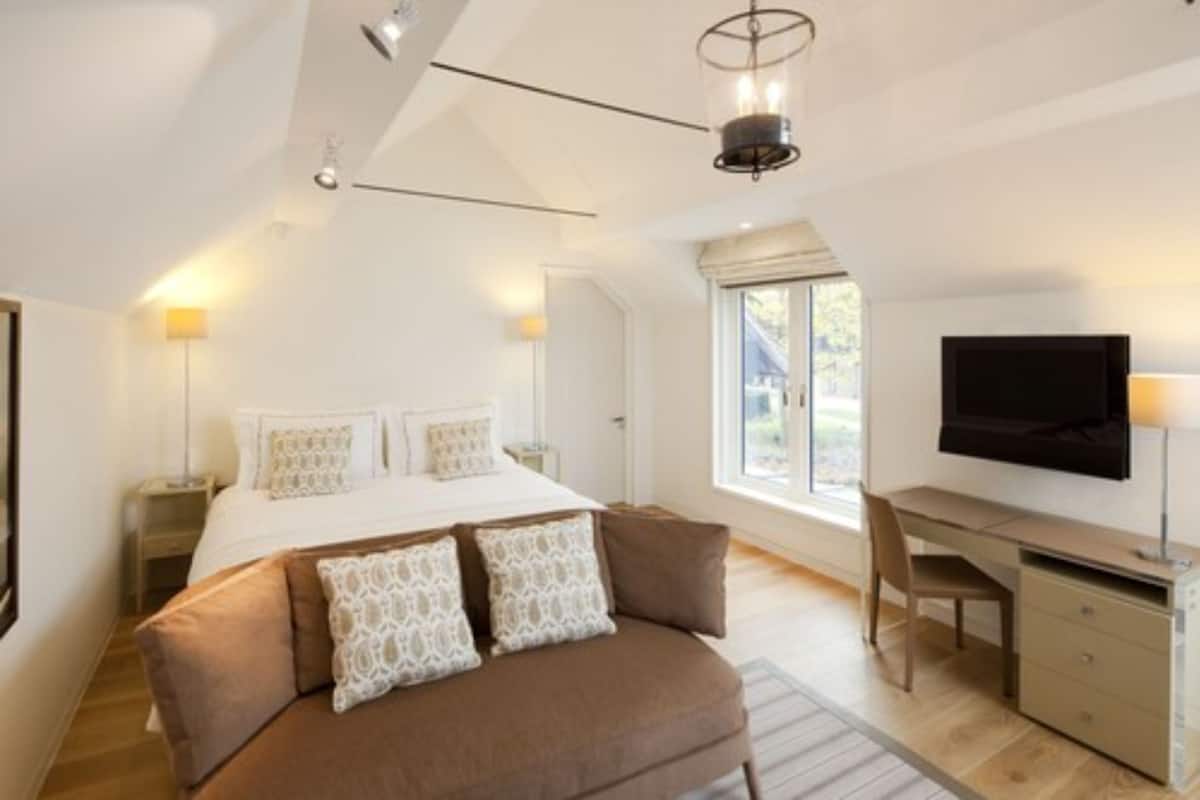 A bedroom with a bed, a desk, a chair, a TV, and a window.