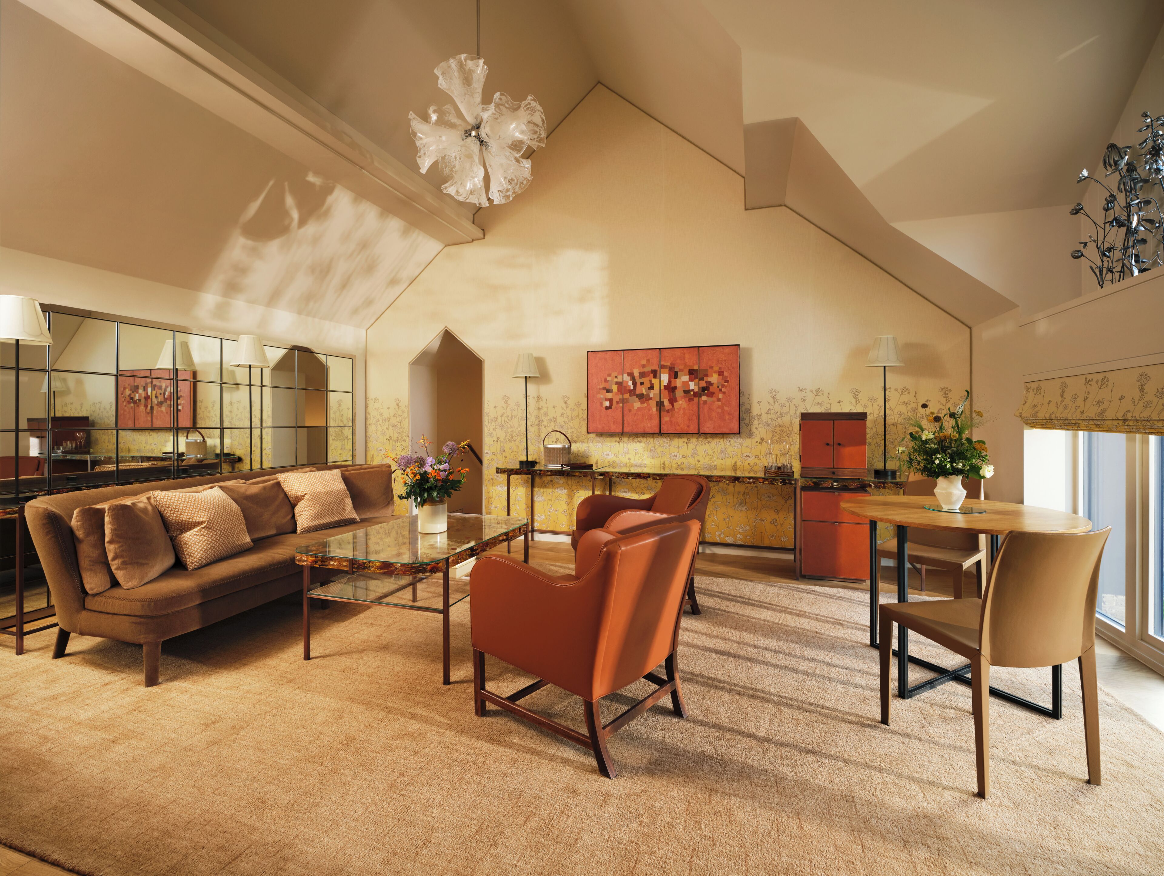 A spacious living area with a high ceiling, a sofa, a coffee table, a dining table with chairs, a kitchen area, and a large window.