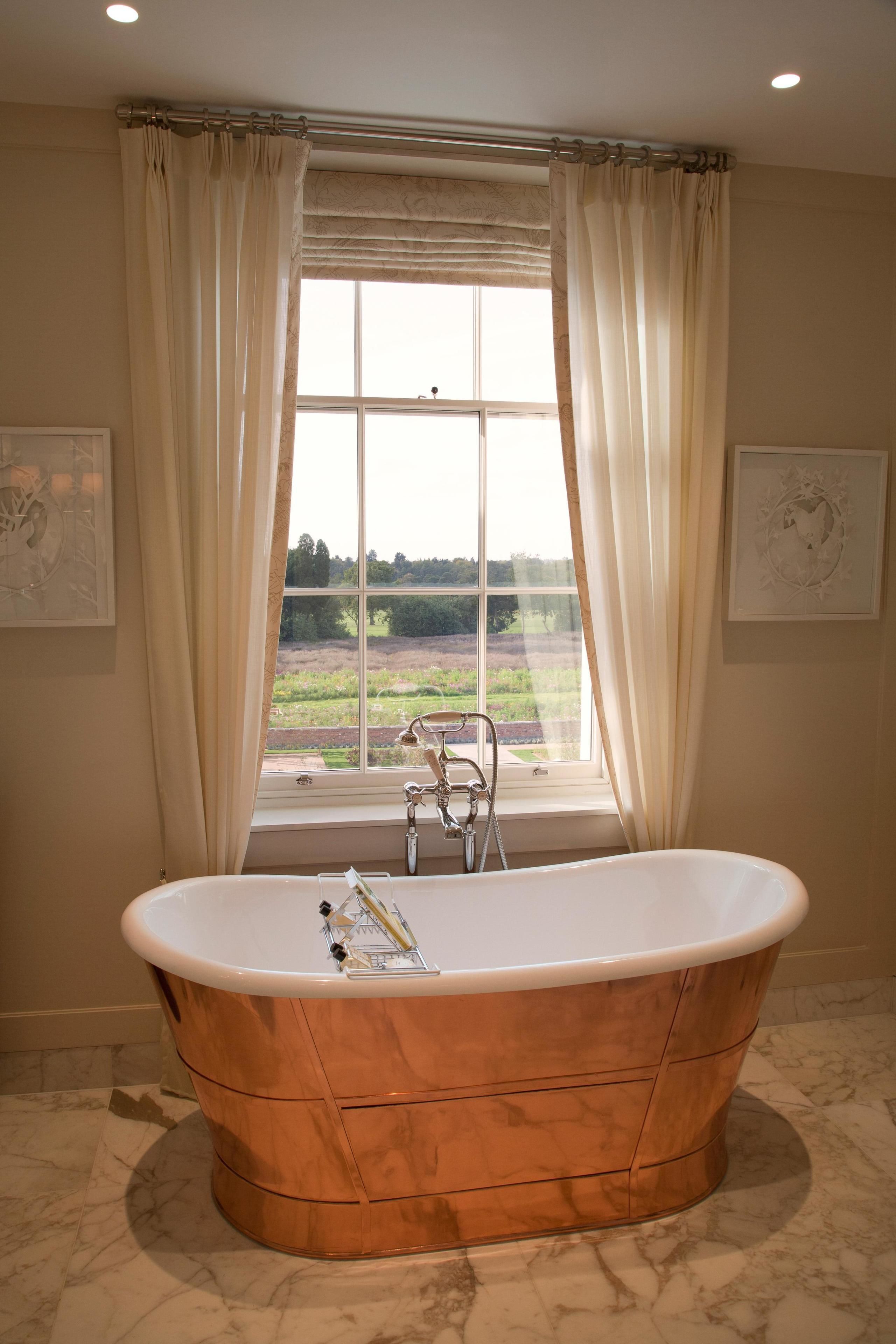 Une salle de bain avec une baignoire sur pieds, une fenêtre avec des rideaux et une vue sur l’extérieur.