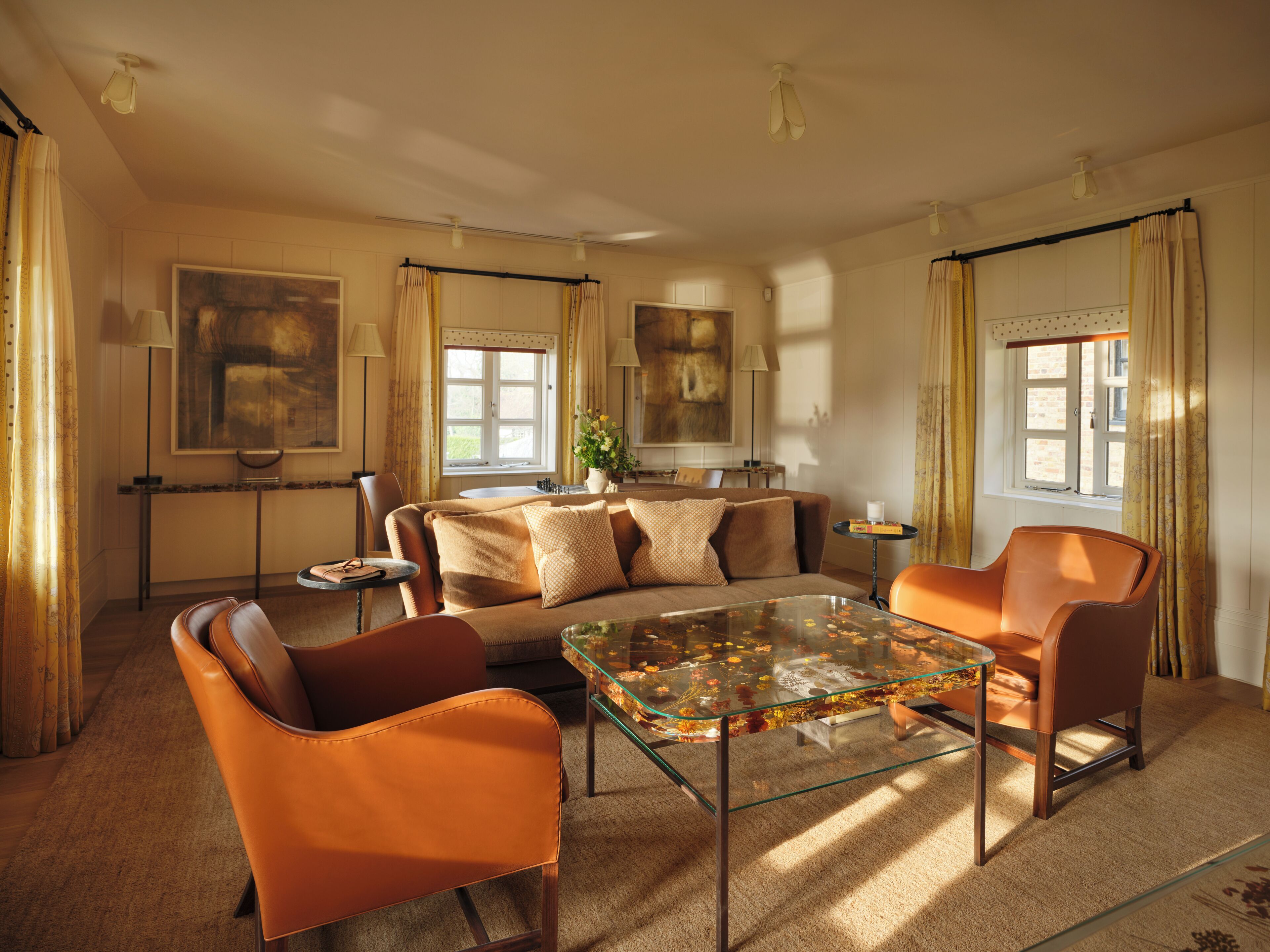 A spacious living room with a glass coffee table, leather armchairs, a sofa, and a dining area.