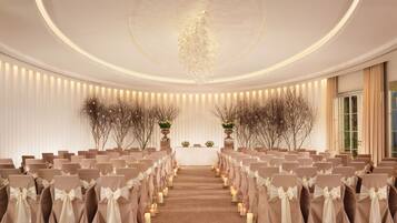 Un espacio para eventos formales con filas de sillas, un pasillo central y elementos decorativos como velas y arreglos florales.