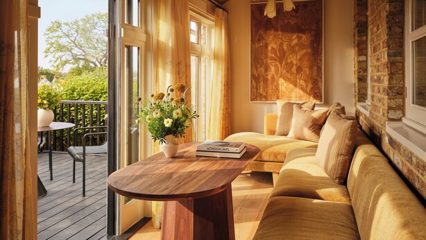 A cozy room with a wooden floor, a sofa, a table with a book, and a window with curtains. - Coworth Park - Dorchester Collection (Ascot)