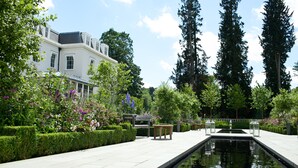 A serene garden with a reflective pool, neatly trimmed hedges, and a white building with multiple windows. - Coworth Park - Dorchester Collection (Ascot)