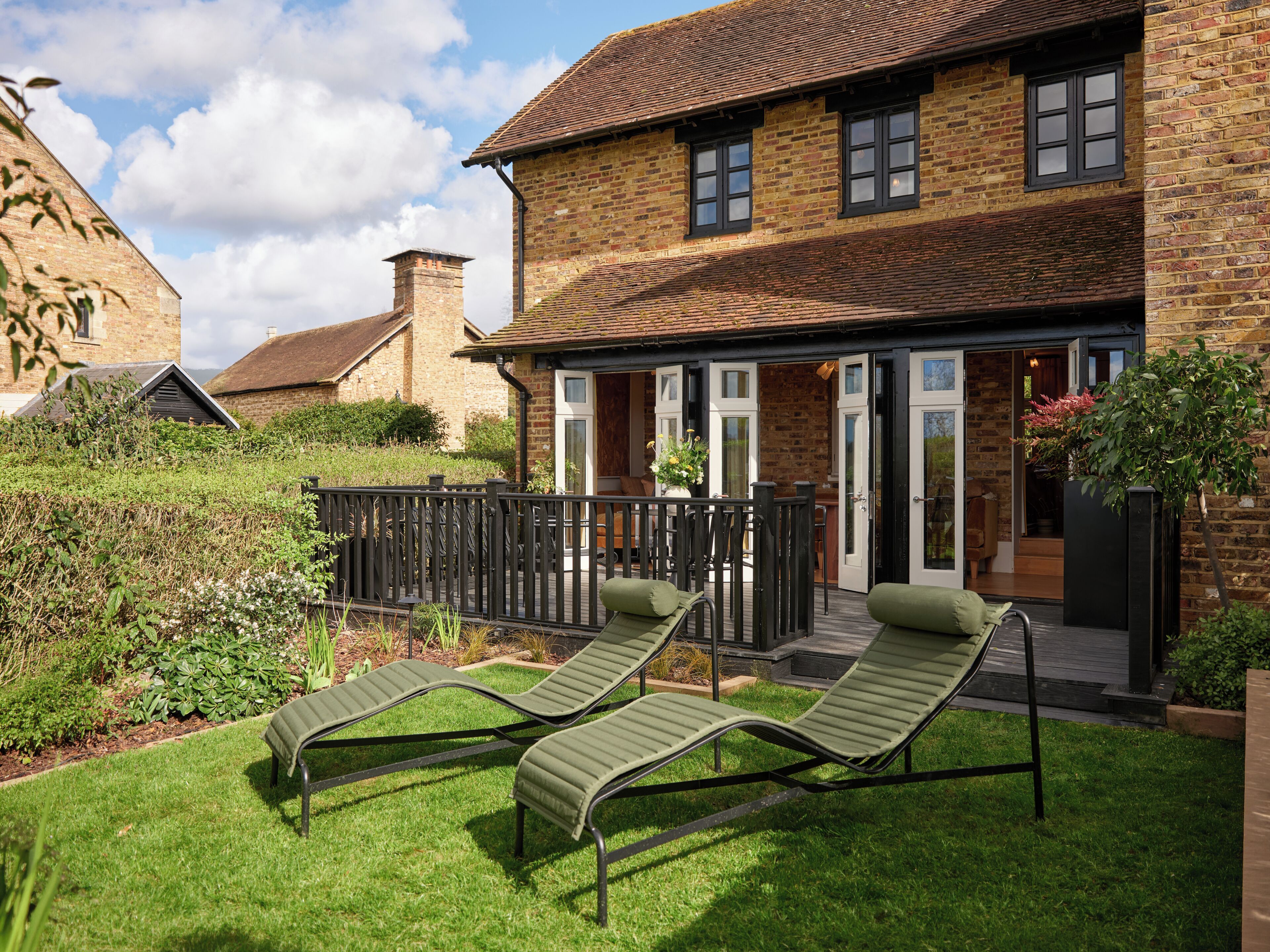 A brick house with a garden, two lounge chairs, and a wooden deck.