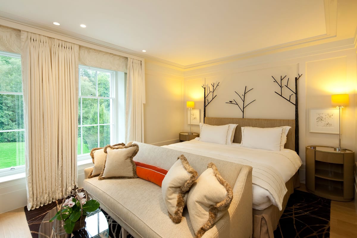 A hotel room with a large bed, a sofa, two bedside tables, and a view of greenery outside.