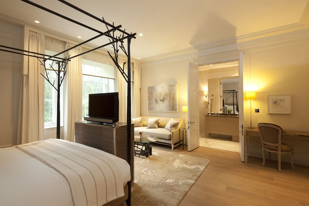 A hotel room with a four-poster bed, a television on a dresser, a sofa, and a desk with a chair.