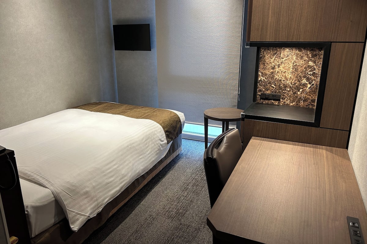 A hotel room with two beds, a small desk, a chair, and a wall-mounted TV.