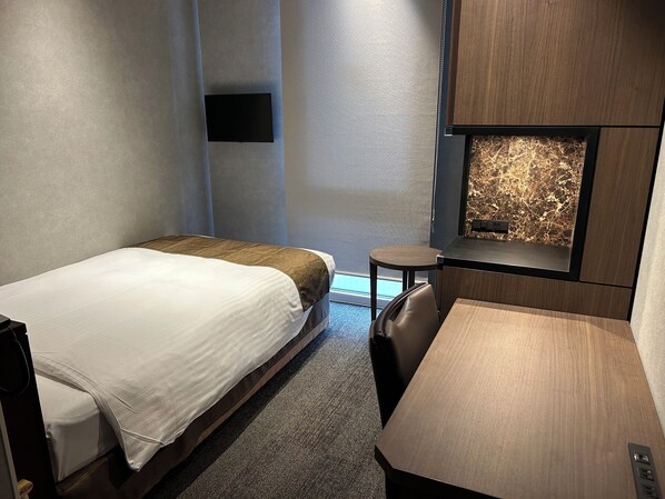 Une chambre d’hôtel avec deux lits, un petit bureau, une chaise et un téléviseur fixé au mur.