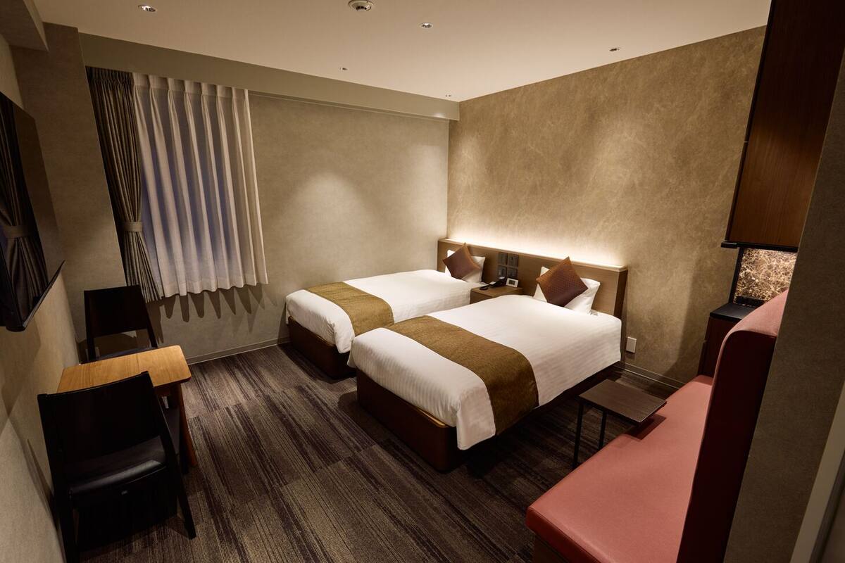 A hotel room with two beds, a desk, a chair, and a small table.