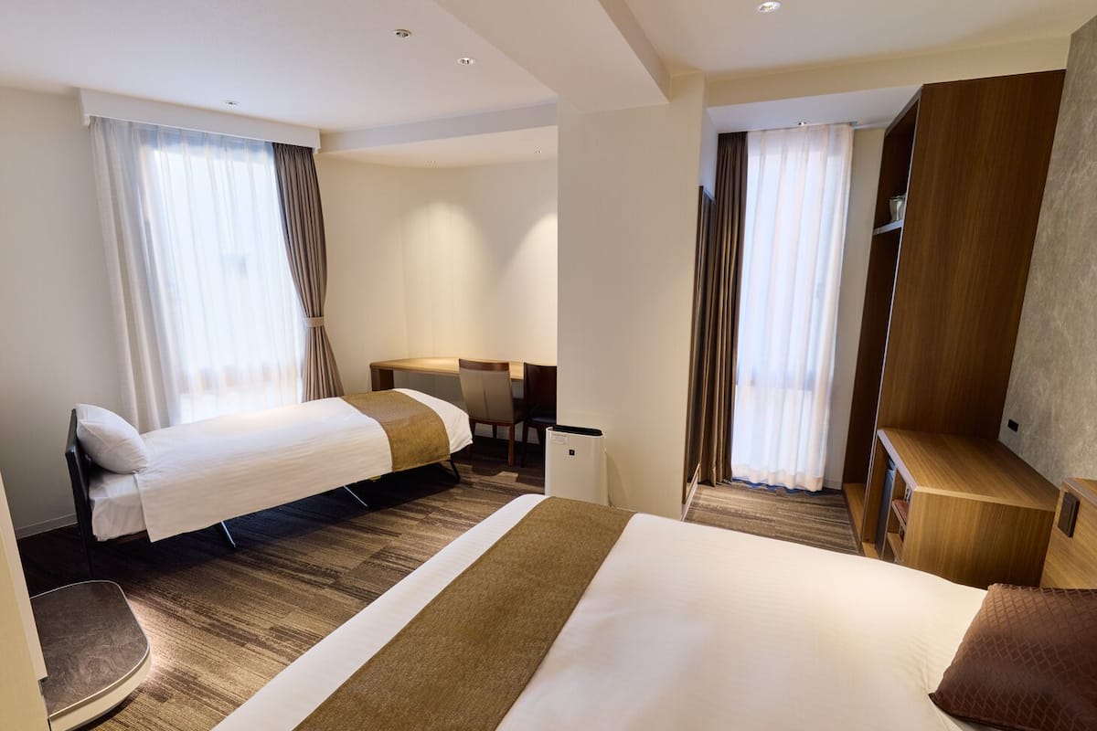 A hotel room with two beds, a desk, and a wardrobe.
