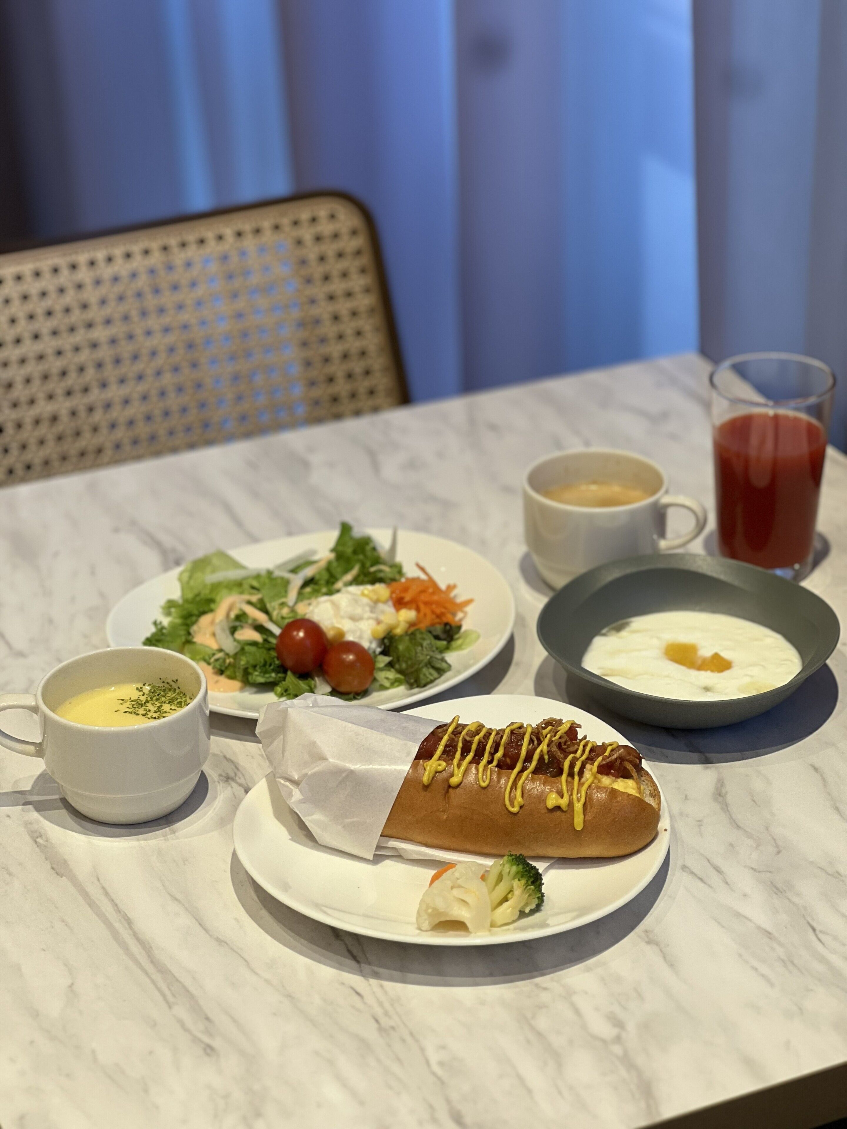 Una mesa de comedor con un plato de comida, una taza de sopa, un vaso de jugo y un bol de huevos.