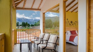 A balcony with a table and chairs, a bed with a red blanket, and a view of mountains. - Killawasi Lodge (Yanque)