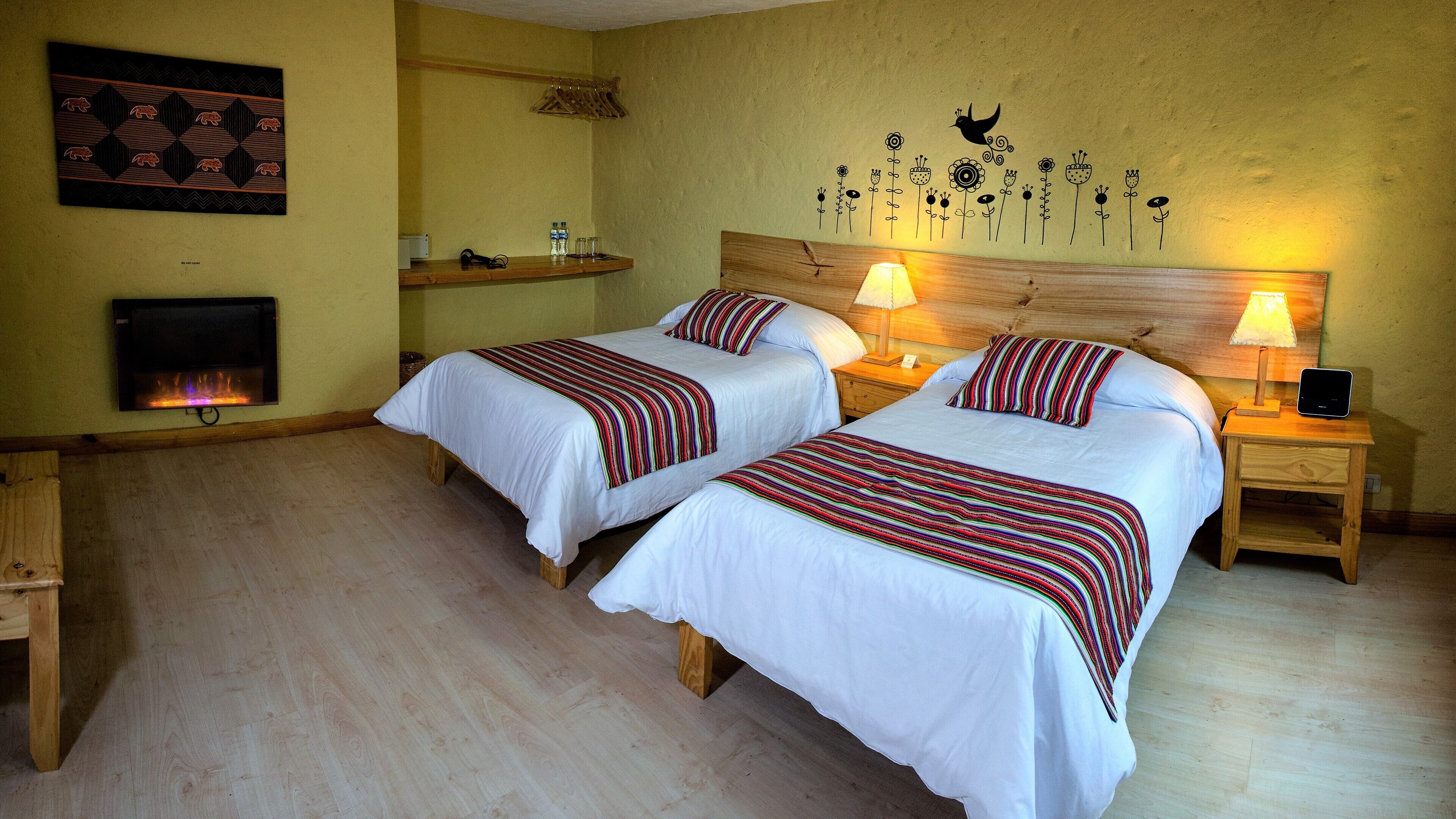 A double room with two beds, a wooden headboard, bedside lamps, a wall-mounted TV, and a fireplace.