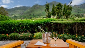 A table with a bottle of champagne, two glasses, and a napkin in a scenic outdoor setting with mountains in the background. - Killawasi Lodge (Yanque)
