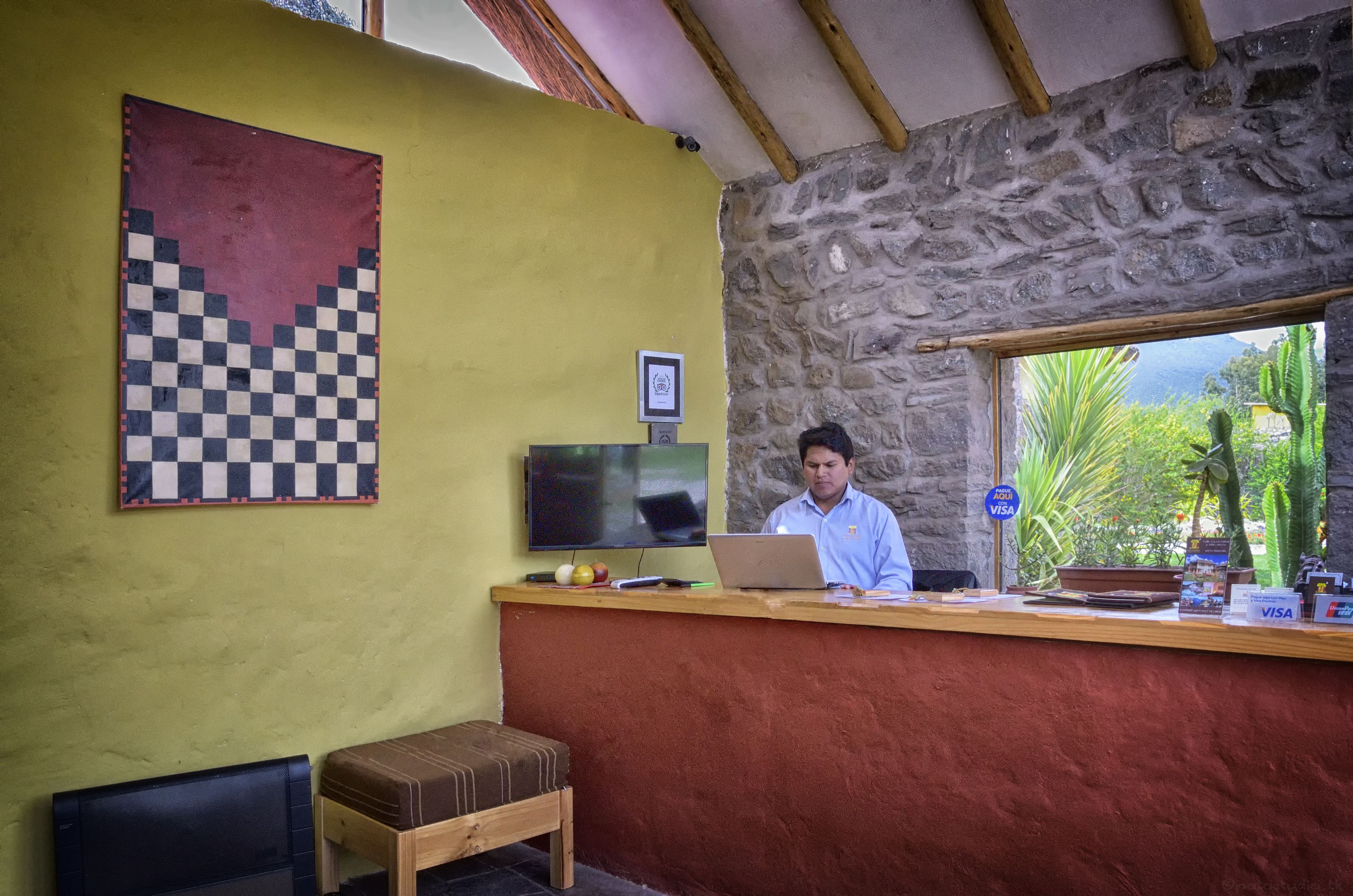 A reception area with a stone wall, a checkered artwork, a television, and a laptop on the counter.