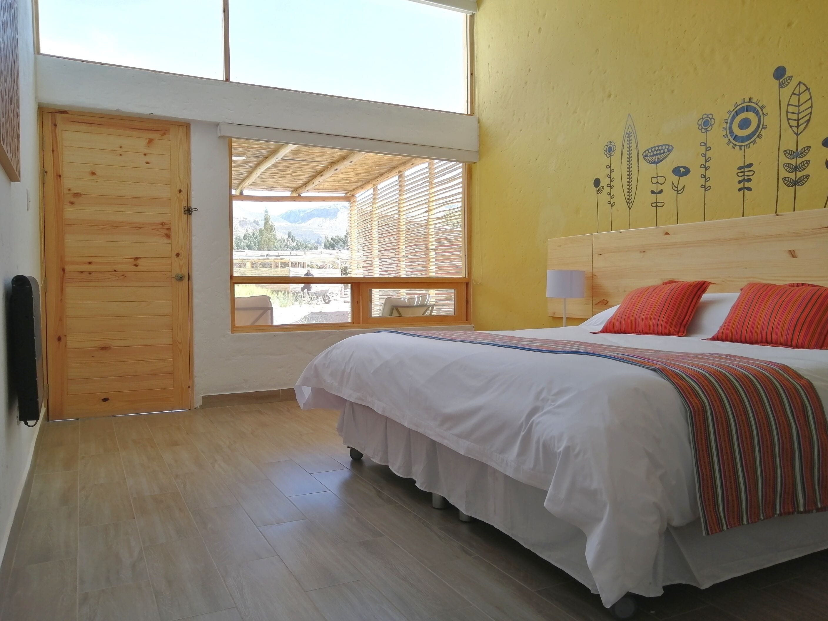 Quarto com cama de madeira, janela com vista e parede amarela com decorações florais.