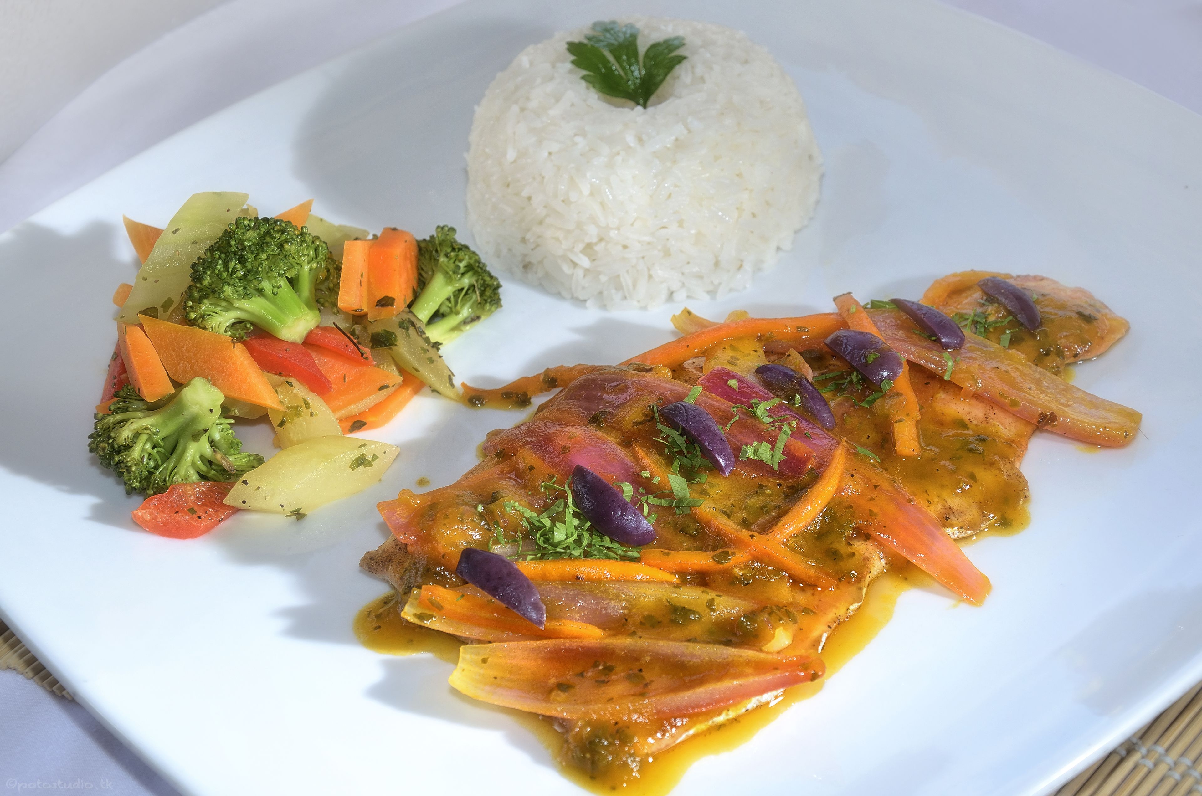 Un plato con arroz blanco, un trozo de pollo con verduras y una guarnición de vegetales mixtos.