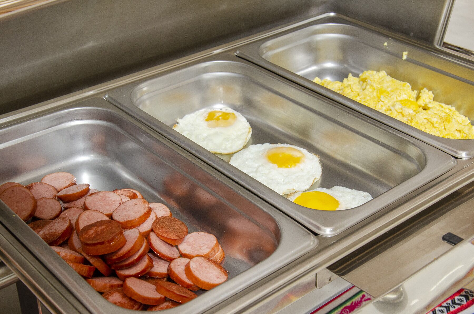 A buffet with sliced sausages, fried eggs, and scrambled eggs.