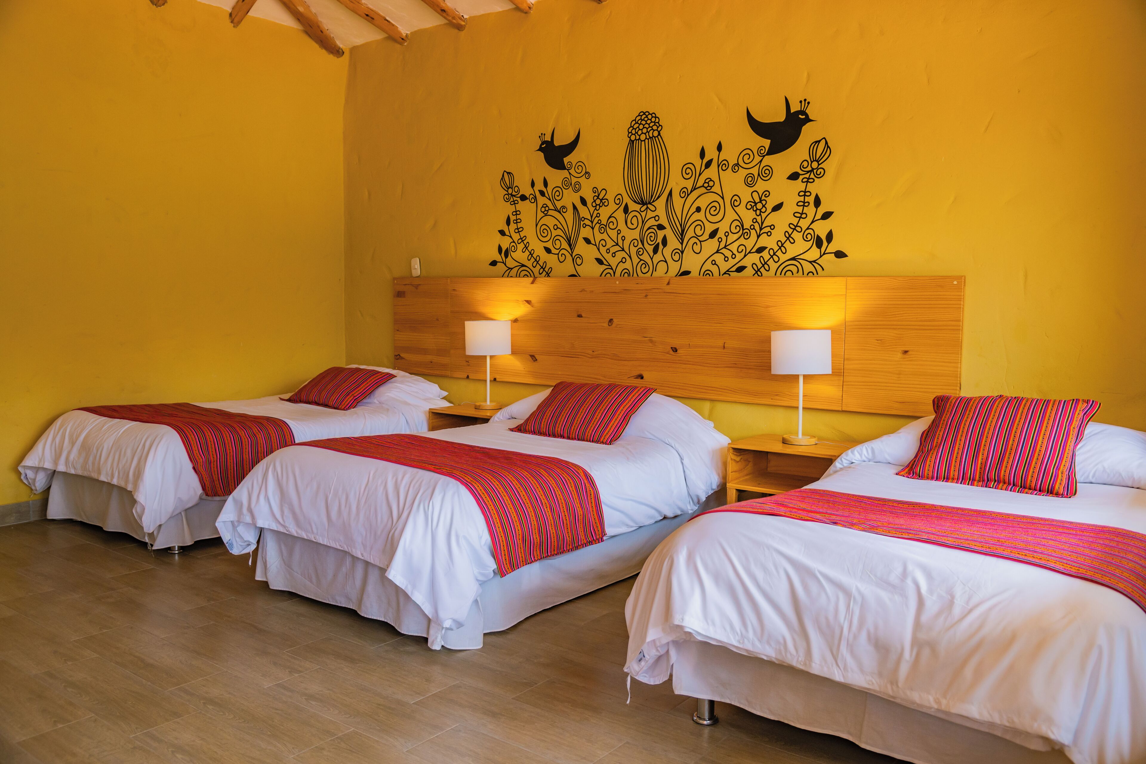 A hotel room with three beds, each with white bedding and red striped blankets. There are wooden headboards and bedside tables with lamps.