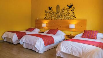 A hotel room with three beds, each with white bedding and red striped blankets. There are wooden headboards and bedside tables with lamps.