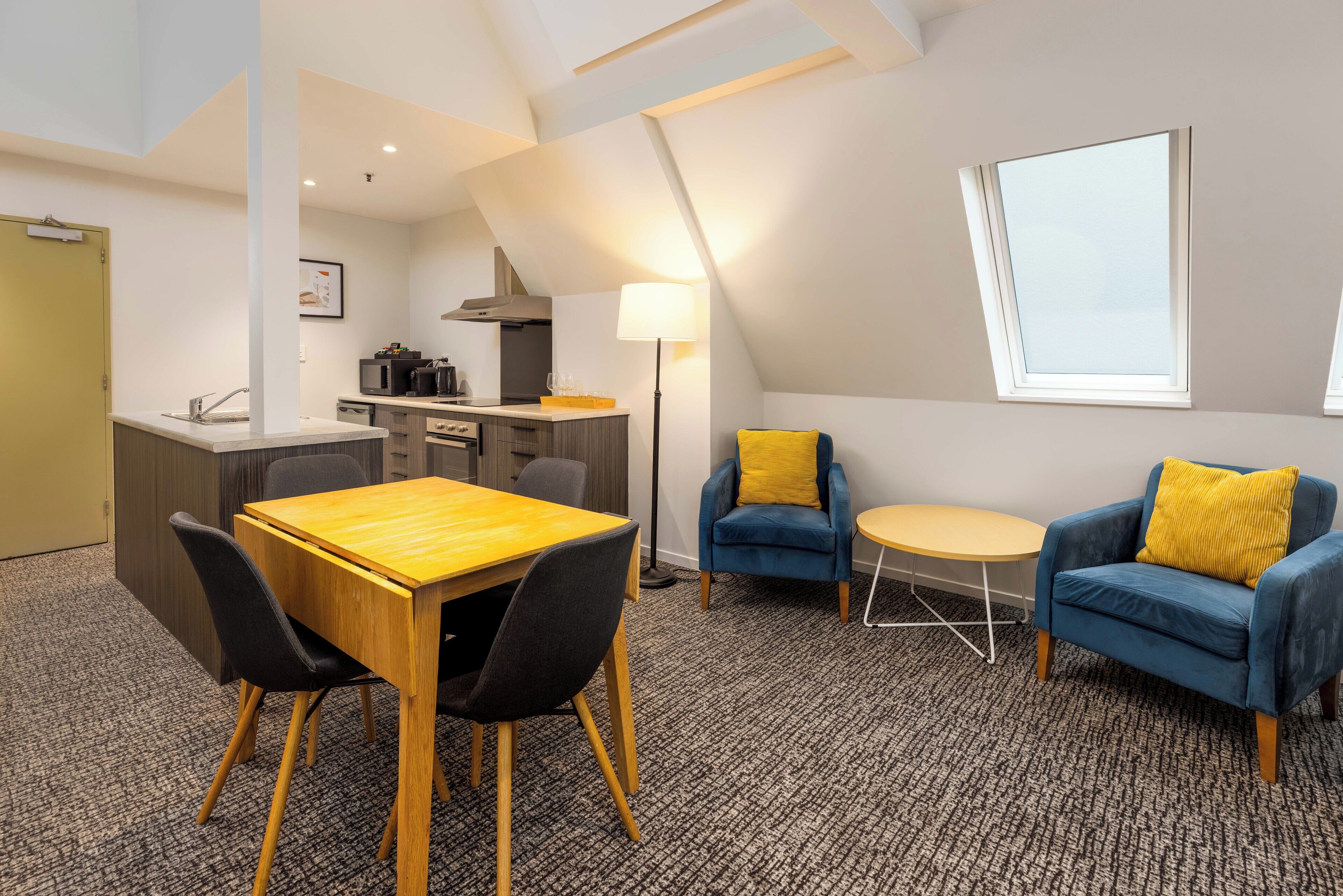 Una habitación de hotel moderna con zona de comedor, sofá y una pequeña mesa.