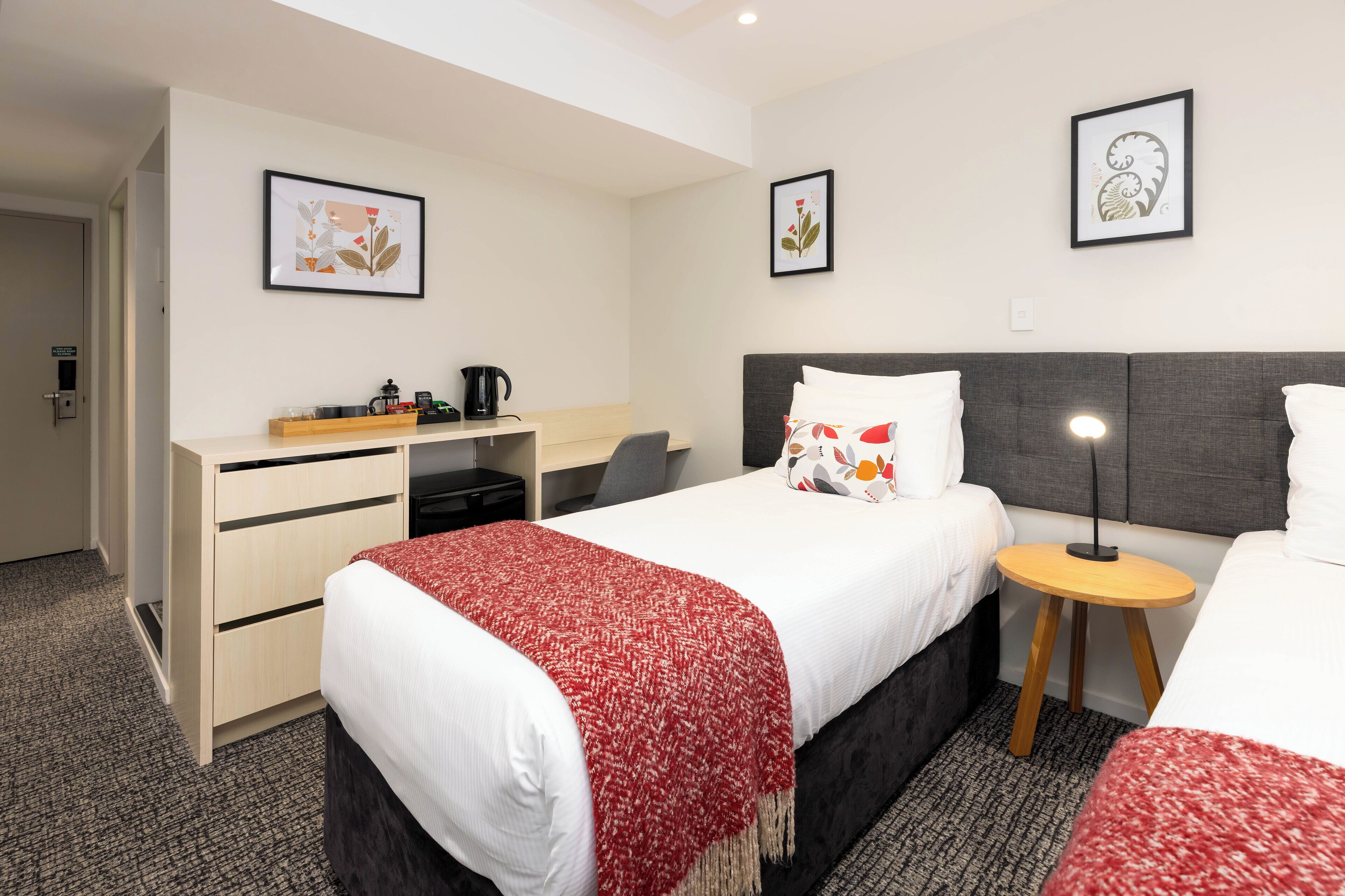 Una habitación de hotel con cama, escritorio, silla, mesita y mesita de noche.