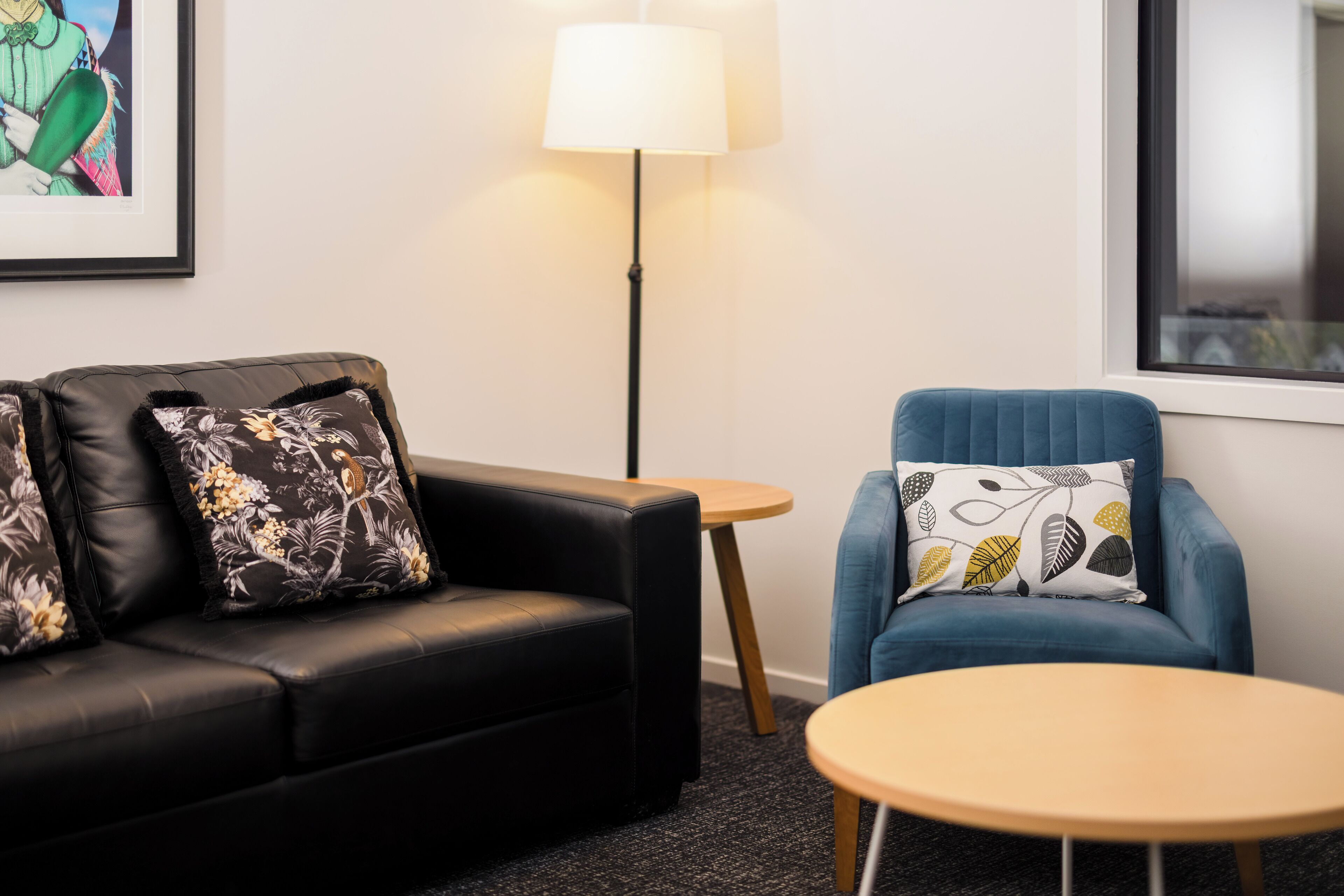 A room with a black leather sofa, a blue armchair, a small round table, and a floor lamp.