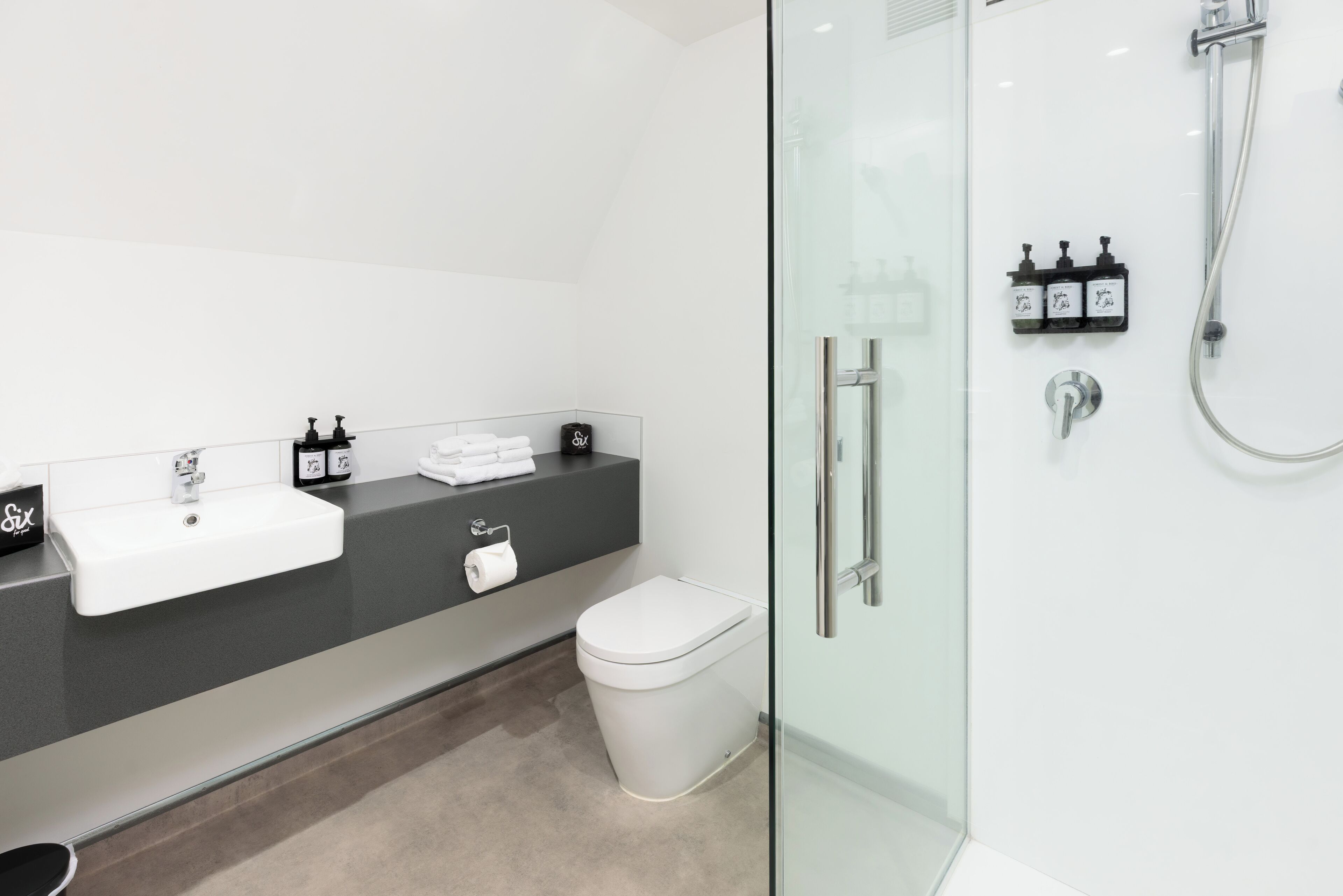 A modern bathroom with a white sink, black countertop, and a glass-enclosed shower area.