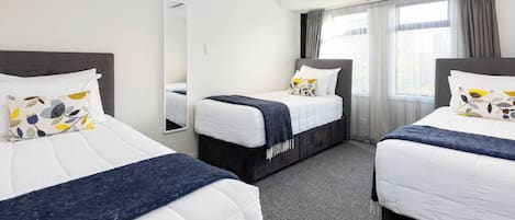 A hotel room with two beds, a large mirror, and a window with curtains.