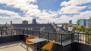 A balcony with two yellow chairs and a table, overlooking a cityscape with historic buildings and modern high-rises. - Hotel Give (Christchurch)