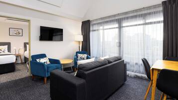 A modern hotel room with a large bed, a sofa, a dining table, and a TV.