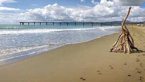 A beach with a wooden structure on the sand, a pier in the background, and footprints leading to the water. - Hotel Give (Christchurch)