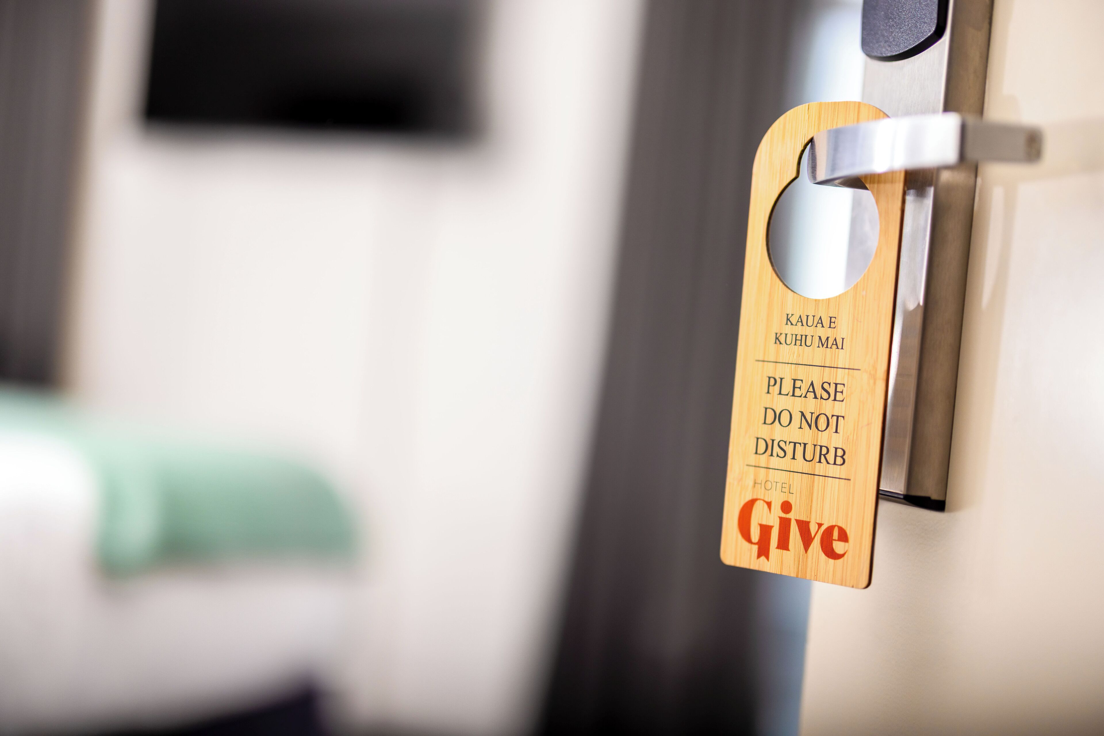 A hotel room door with a wooden sign that reads 'Kauae Kuhu Mai' and 'Please Do Not Disturb.'