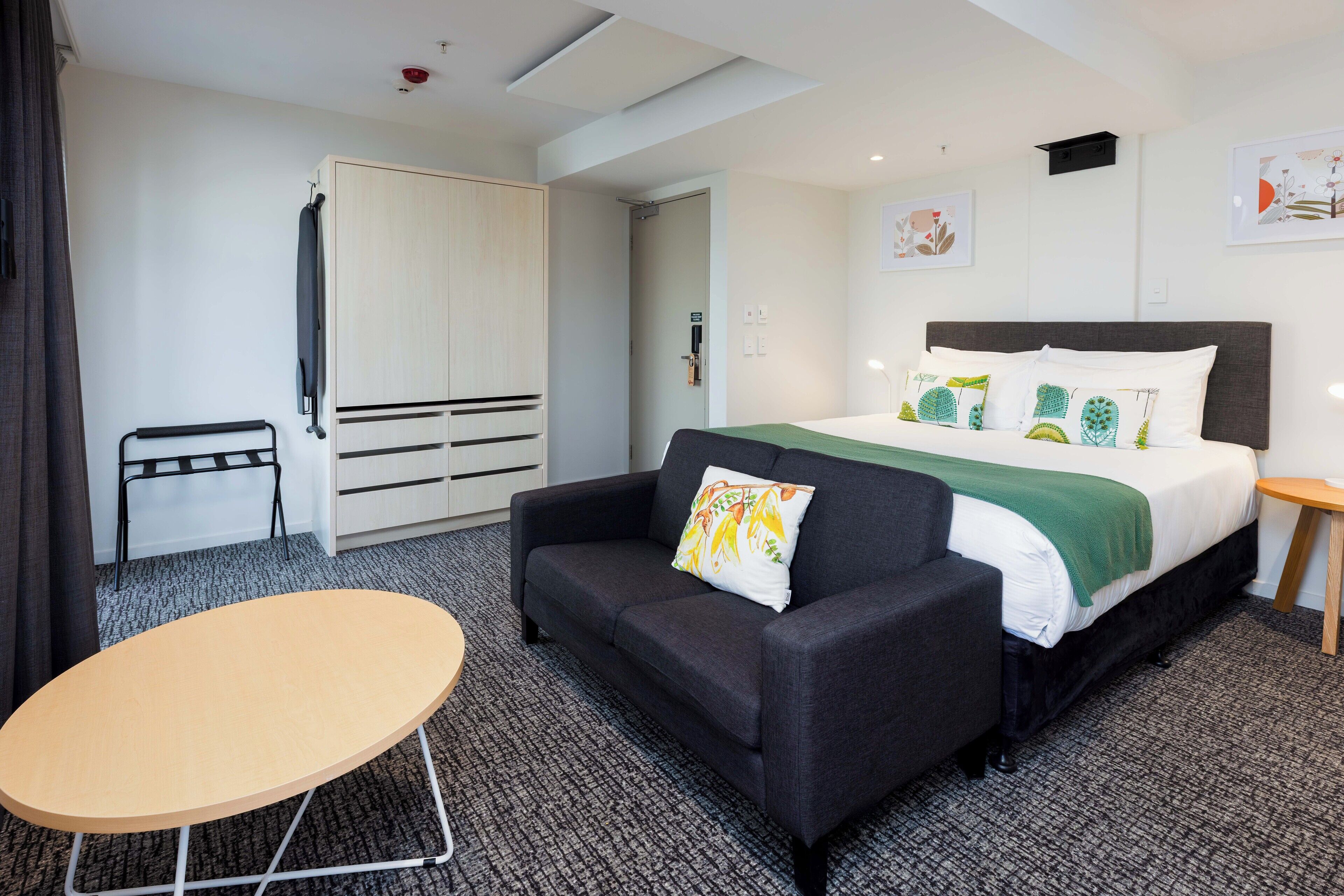 A hotel room with a bed, a sofa, a small table, a wardrobe, and a door.