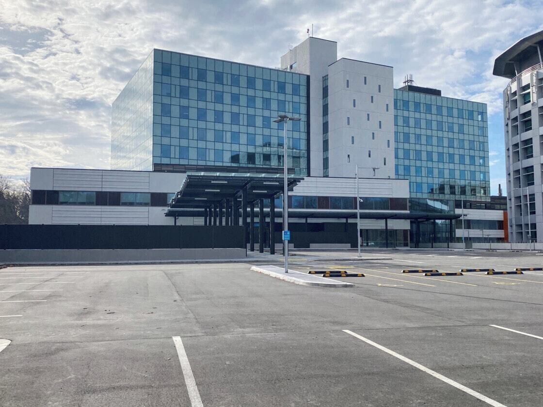 A modern building with a glass facade, a covered entrance, and a parking lot.
