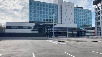 A modern building with a glass facade, a covered entrance, and a parking lot.